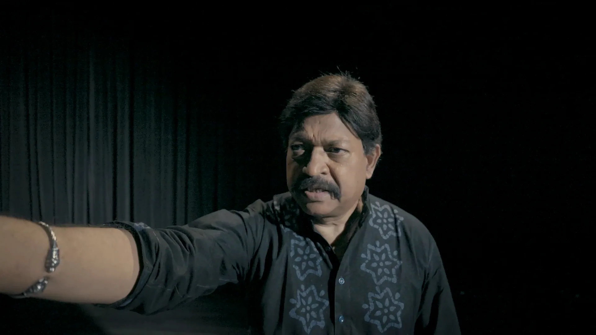 Om Katare as Yash Kirti on a dark stage, one arm outstretched