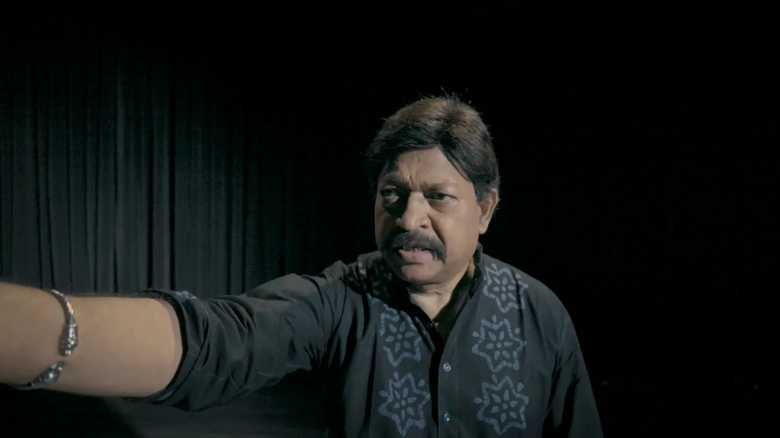 Yash Kirti performs on a dark stage, one arm outstretched