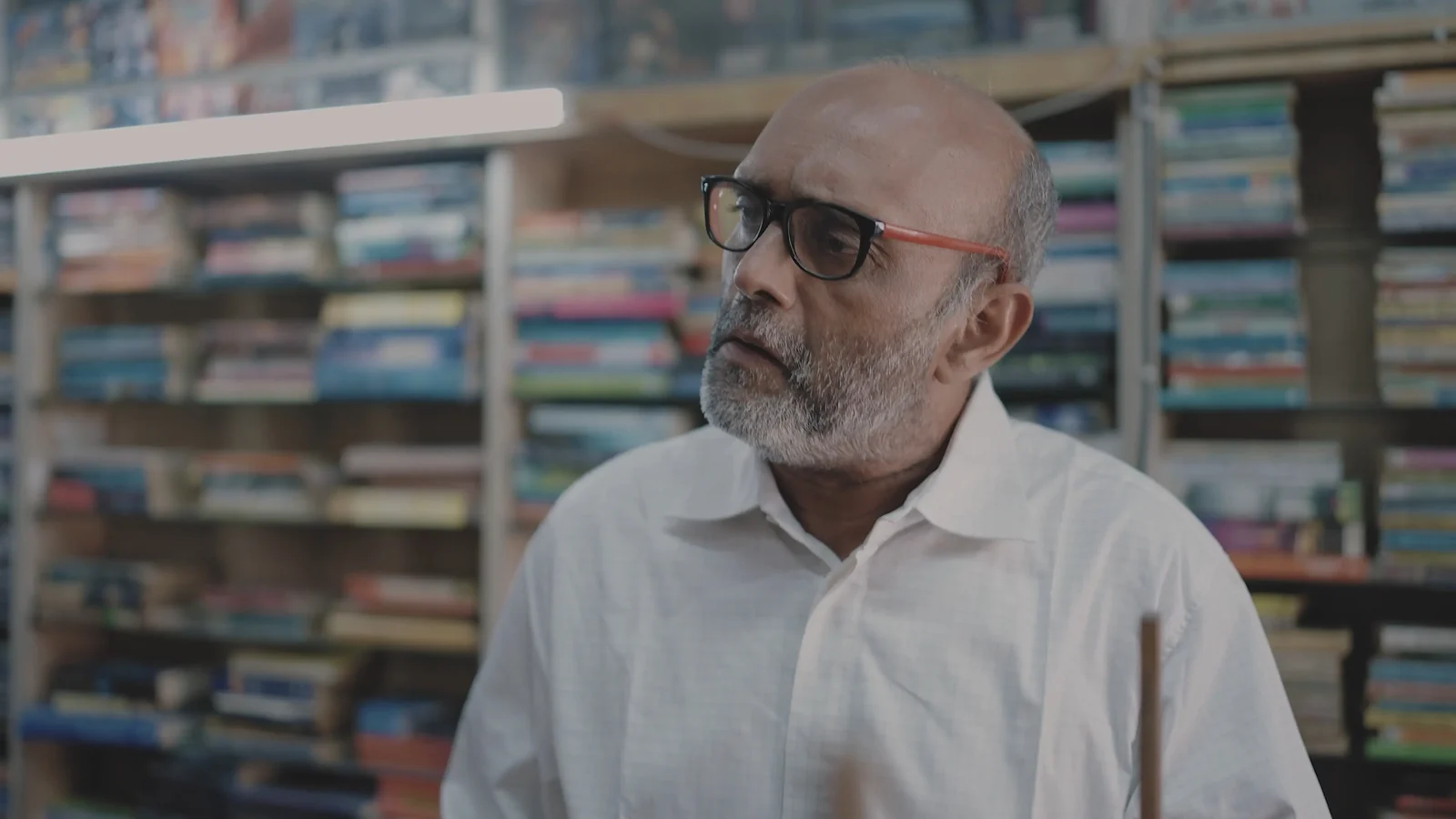 Akbar Hussain as Shamji Bhai, in the bookshop.