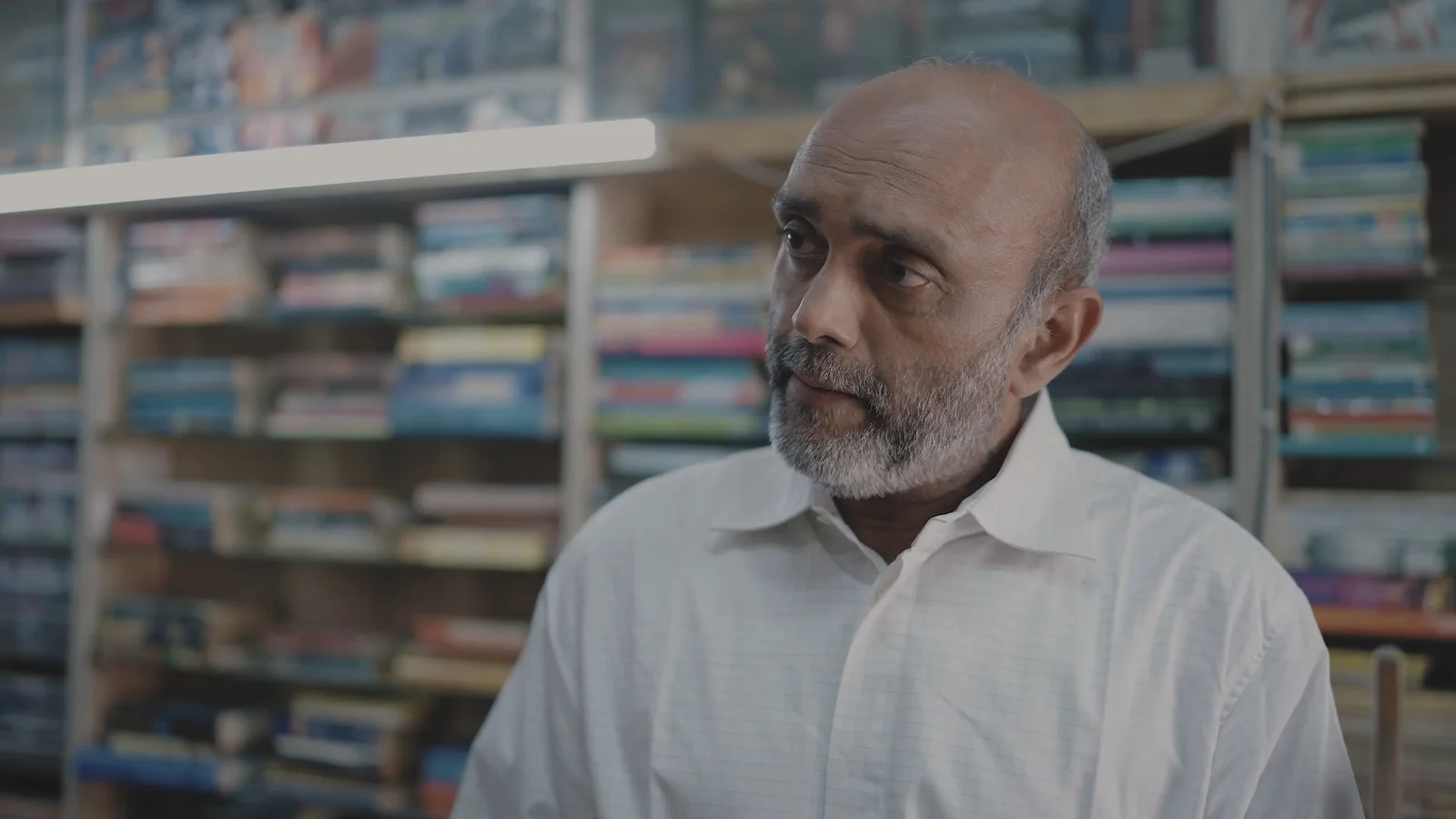 Akbar Hussain as Shamji Bhai, in the bookshop.